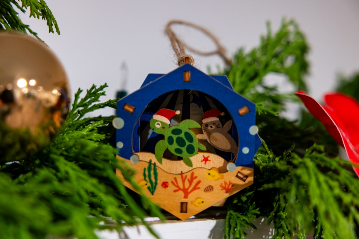 Decorative 3D Christmas ornament with a turtle and monk seal design on a green tree.