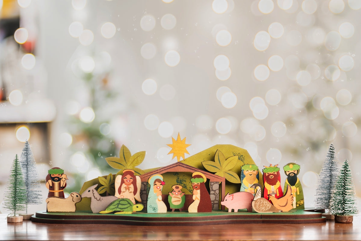 A wooden nativity scene set featuring cut-out letter shapes with figures of Mary, Joseph, and baby Jesus, along with other nativity characters, all crafted in a tropical theme with green and brown colors, in front of sparkle bokeh backdrop.