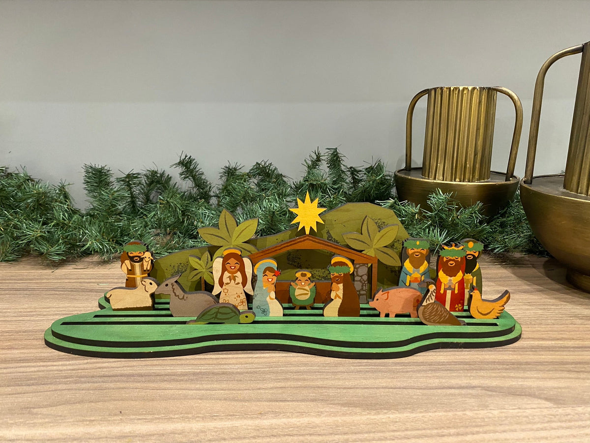 A wooden nativity scene set featuring cut-out letter shapes with figures of Mary, Joseph, and baby Jesus, along with other nativity characters, all crafted in a tropical theme with green and brown colors.