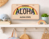 Decorative license plate with rainbow and 'Aloha' text on a shelf with decorative items.
