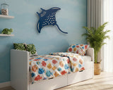 Children's bedroom with a bed featuring fish-patterned bedding, a blue stingray wall decoration, and a plant.
