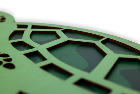 Close-up of a green decorative wood turtle cutout with geometric cut-out patterns on a white background